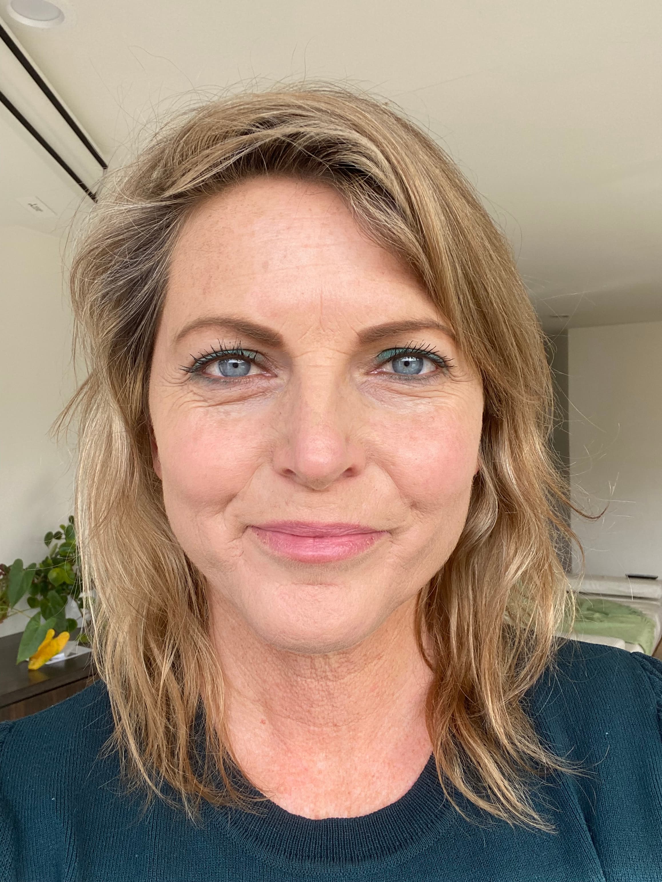 Close-up of a blonde woman with blue eyes and teal eyeshadow smiling slightly.